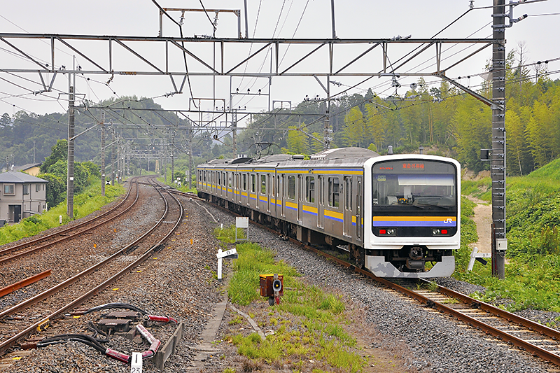 外房線下りホーム千葉寄り端から土気駅方向を眺めたところ。右の209系電車が走っている線が現在の東金線へと接続する線路で、左のカーブした複線が外房線。東金線側が元々は直線で延びていたであろうことが窺われる点からも、こちらが本来の主本線であったことが察せられるだろう。ちなみに、1972年5月26日の大網駅移転前夜までの旧線は、この辺は単線で使用していたという点も加味しと眺めると当時の姿を連想しやすい。