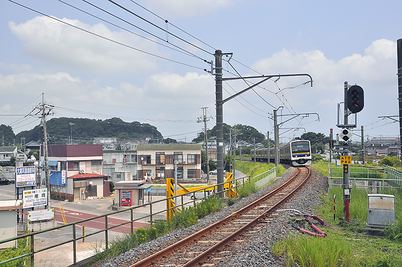 東金線ホーム成東寄り端からの眺め。209系電車が走っている線路が外房線に直通できる4番線で、右にちらりと見える線路が行き止まりの3番線。東金線は左に大きくカーブをして、左隅の丘が少し窪んでいる所を線路が通っている。