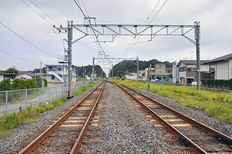 上写真の同じ踏切から反対側の成東方を眺めたところ。左の青い屋根の建物がJR東日本 大網保線技術センターの建物で、その前に3番線と4番線の分岐器が配置されている。