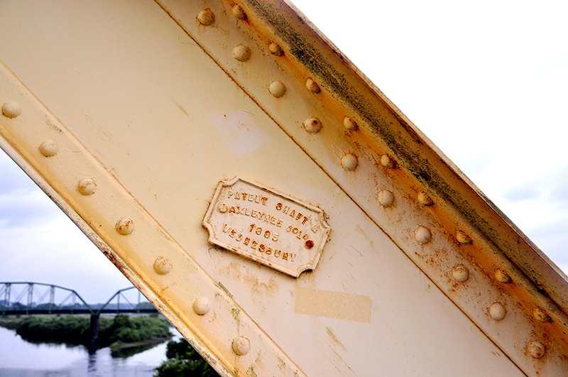 1886年英国パテント・シャフト&アクスルトゥリー社製の銘板。なぜか斜めに貼られている物がある。左下に見えるのは樽見鉄道の揖斐川橋梁。