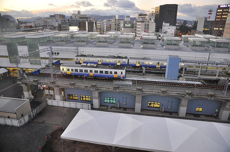 取材日は、駅の東隣に建つホテルエコノ福井駅前の8階の部屋が取れたので、そこからの俯瞰写真3枚で仮福井駅の構造を見ていこう。まずは南側車止め部分。プラットホームよりさらに線路が2両分延びており、電車が留置できるようになっている。