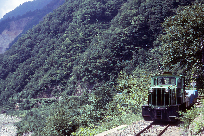 1982年7月頃の立山砂防軌道の列車走行風景。とはいっても線路端で撮ったのではなく、前走列車内から続行列車を撮った写真。左に大崩落の痕が窺えるが、沿線にはこのような場所がたくさんある。