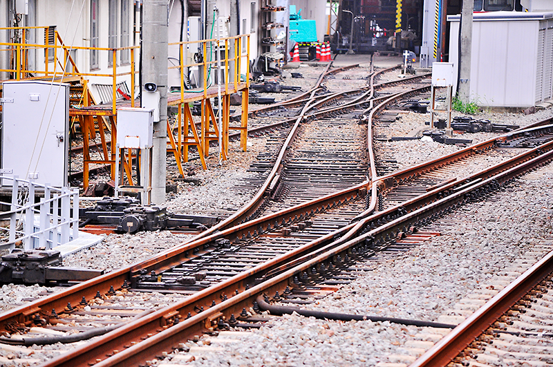 手前は入生田駅2番線(山側)3線軌条から車庫へと1,435mmゲージのみが分岐している分岐器。営業列車が通る直線1,067mmゲージ側ではレール密着部分とクロッシングの数が通常の分岐器と同じなので、独特の通過音は期待できない。