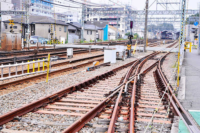 京急線の1,435mmゲージと総合車両製作所横浜事業所専用線の3線軌条が分岐する分岐器の背向からの眺め。共通レールの延長上にある直線側に固定クロッシングが2つ入っている。