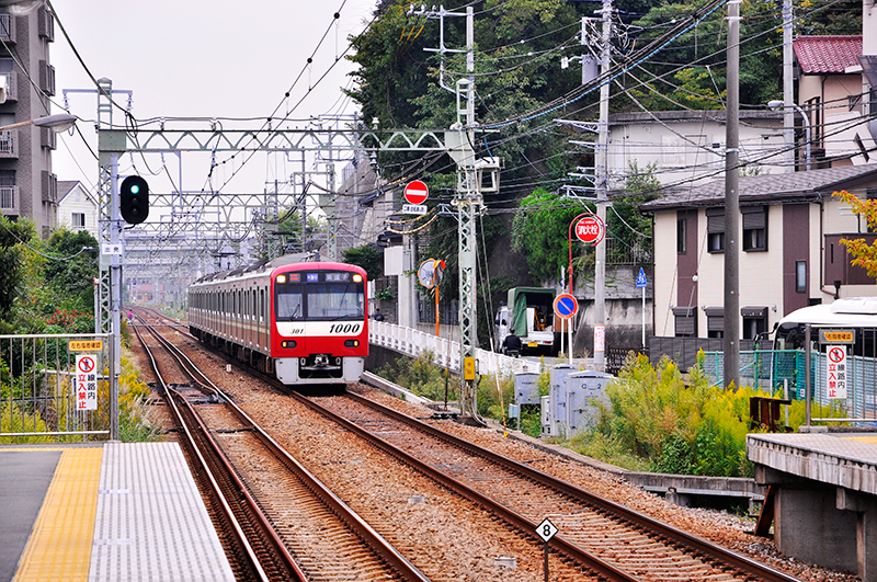 六浦駅2番線から金沢八景駅方の眺め。新1000形1301の先頭あたり左の上り線に設置されているのが特殊分岐器。これによりプラットホームを改良して車輛との隙間を狭ばめられた。