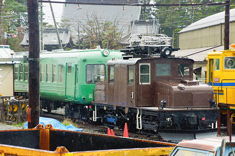 新村駅プラットホームから松本寄りのクハ5006を眺めたところ。2015年の状況ではあるが、手前に電気機関車が留置されていたので、前面がよく見えないのが残念。ちなみにこの機関車はED30形ED301で、大元は1927年(昭和2年)アメリカ製の信濃鉄道1形3という、こちらも貴重な車輛。2005年9月に除籍され、その後に静態保存へと移行している。