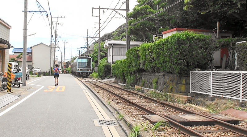 極楽寺-稲村ヶ崎 間の併用軌道で、極楽寺駅寄りからの稲村ヶ崎駅方の眺め。線路と道路の間の縁石がコンクリート地のまま(2016年1月時点)なのもあるため、これぞ路側軌道という光景が展開している。車輛は2000形電車。