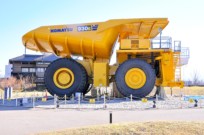 KOMATSU930Eの右サイドビュー。ベッセル(荷台)は丸底タイプを装備。これにより、衝撃による変型に強くなっているとのとこ。背後に見える建物は『わくわくコマツ館』で、小松製作所 旧本社建屋を再現した外観だそうだ。