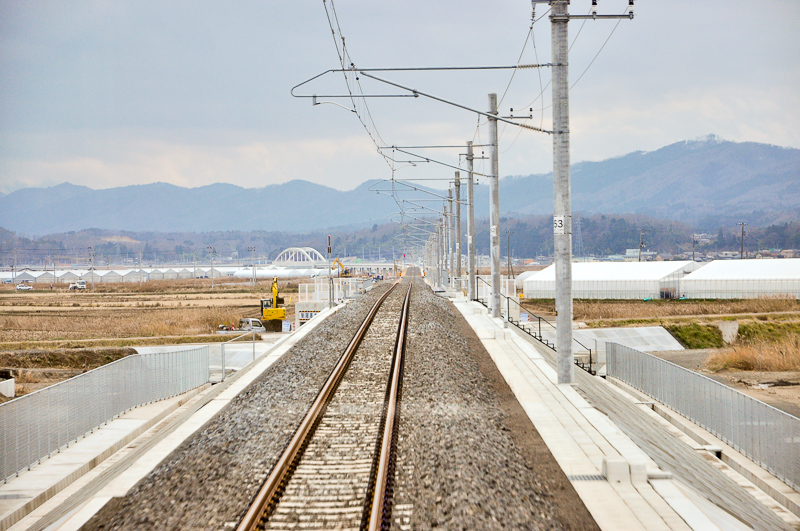 新線に入ってからは築堤になり、さらに高架線で田園地帯を抜けてゆく。写真中央やや左の橋梁は、浜吉田駅から駒ヶ嶺方に約3km程の地点にある下路式アーチローゼ橋。