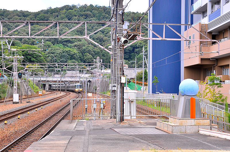 新逢坂山トンネルを抜けて、京都方から大津駅へ進入する223系使用の新快速。写真では新逢坂山トンネルの坑門は跨線橋のさらに先にあるため見えないが、複々線の線路のうち左の下り線2本が1921年に開通した方のトンネルへと続く線路になる。ちなみに、右にある丸いモニュメントは『北緯35度と大津駅』の碑。