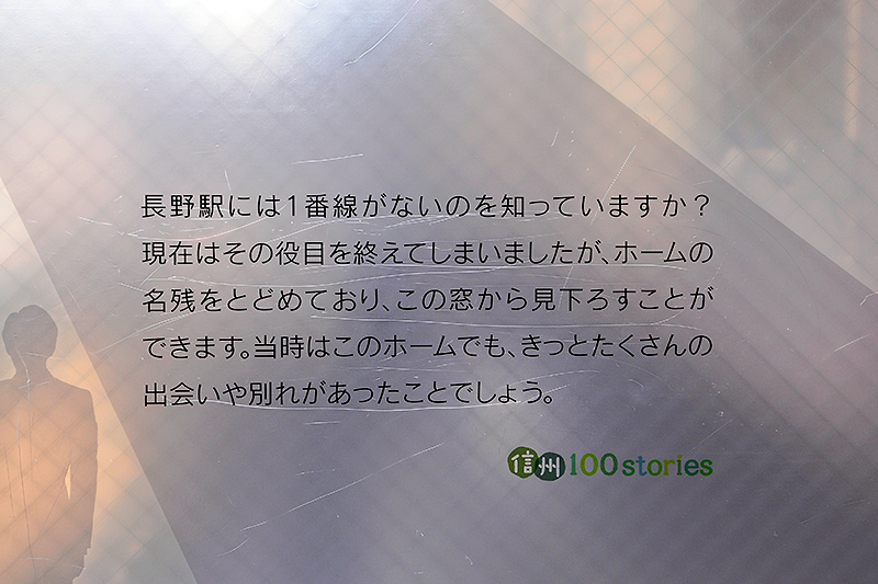 装飾ガラスのホーム上屋部分に書かれた説明文。「信州100stories」プロジェクトの一環なのが解る。